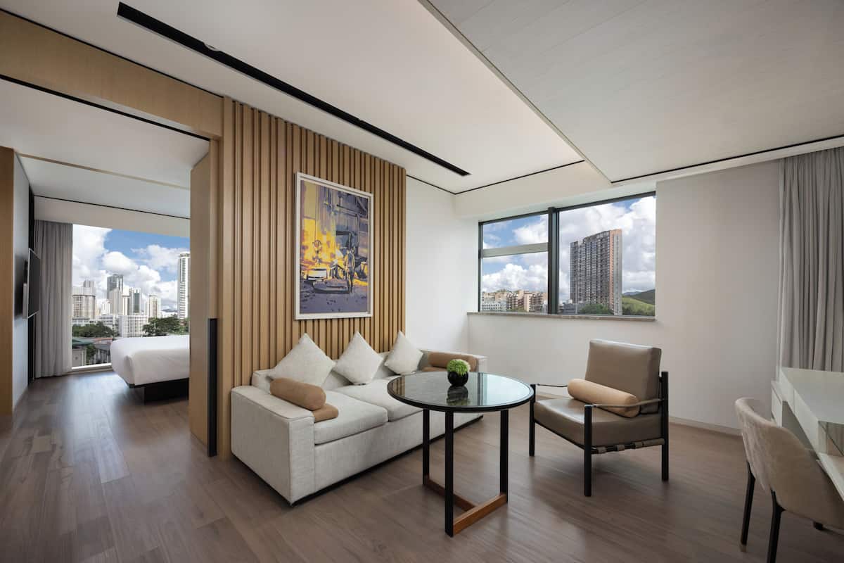 Habitación de hotel moderna con sofá, sillones, una mesita y un amplio ventanal con vistas a la ciudad.