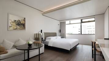 A modern hotel room with a bed, a sofa, a small table, and a large window.