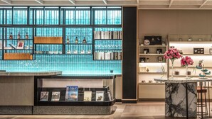 A modern hotel lobby with a bar area, bookshelves, and a seating area with bar stools.