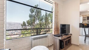 A modern living room with a large window, a flat-screen TV, a radiator, and a small round ottoman. - Amazing view in Cusco (Cusco)
