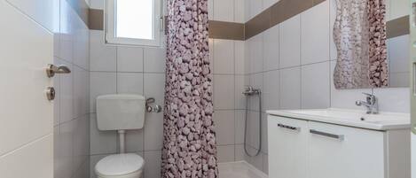A bathroom with a toilet, shower, and sink.