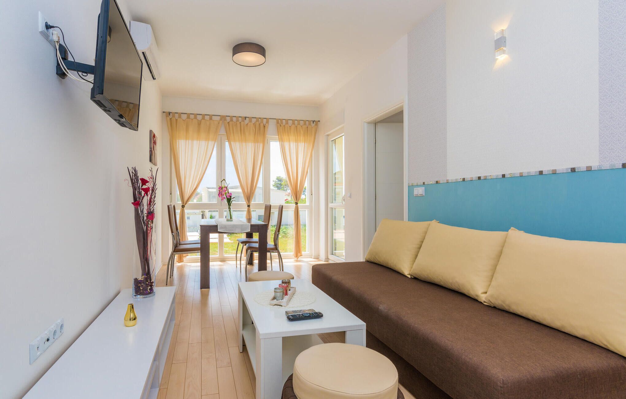 Uma sala de estar moderna com um sofá marrom, uma mesa de centro branca e uma área de jantar com mesa e cadeiras.