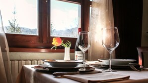 A dining table set with plates, glasses, and cutlery, a bottle of wine, and a vase with a flower, by a window with a view of the outdoors. - Le Stanze della Musica (Borgomale)