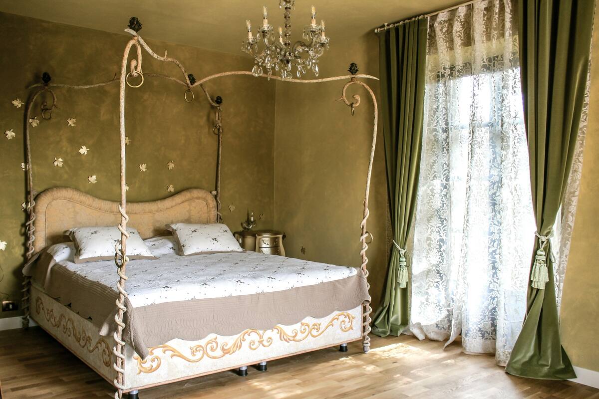 A four-poster bed with a chandelier, a nightstand, and a window with curtains.