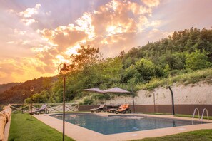 A swimming pool with lounge chairs and umbrellas, surrounded by a landscaped garden and a hillside.
