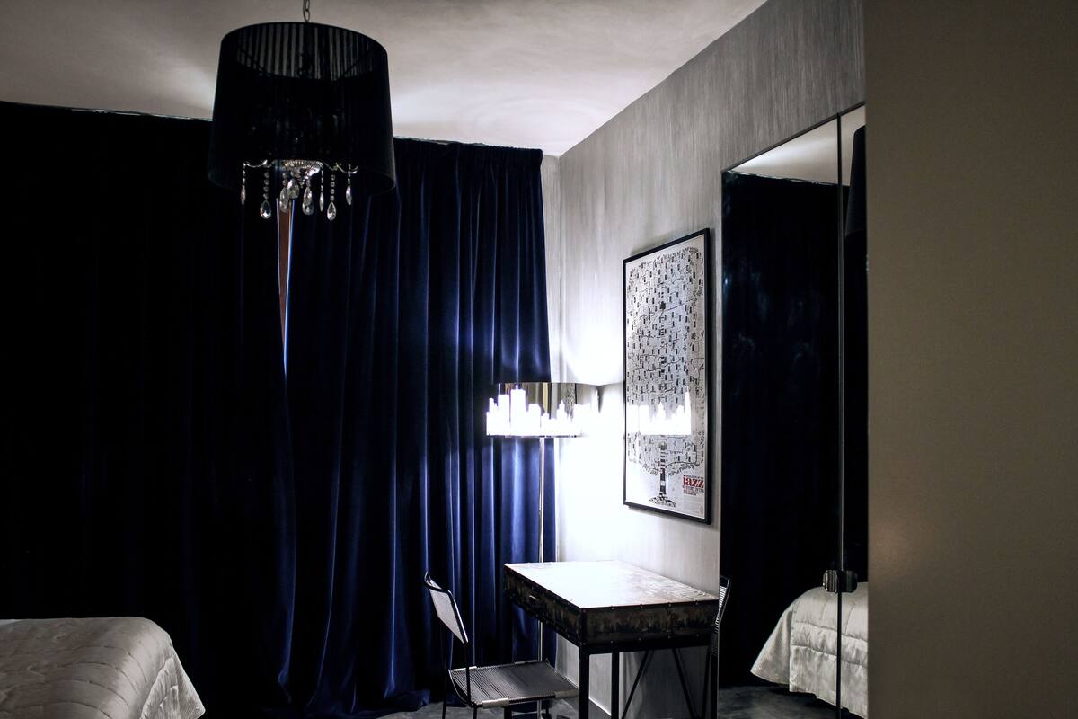 A hotel room with a large bed, a desk, a chair, a chandelier, and a framed picture on the wall.
