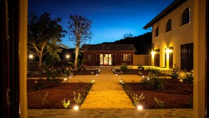A courtyard with a stone pathway leading to a building with a tiled roof and large windows. - Le Stanze della Musica (Borgomale)