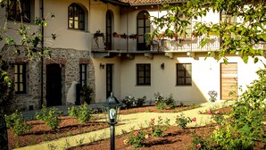 A two-story building with a stone facade, multiple balconies with plants, and a garden with roses. - Le Stanze della Musica (Borgomale)