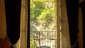 A balcony with a chair and table, curtains, and a view of trees. - Le Stanze della Musica (Borgomale)
