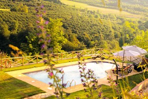 Una piscina con cubierta de madera y sillas de descanso, rodeada de un paisaje verde exuberante.
