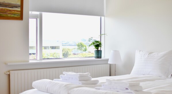 A hotel room with a large window, a radiator, a bedside table with a lamp, a bed with white linens, and a potted plant on the windowsill. - Nes Residence (Seltjarnarnes)