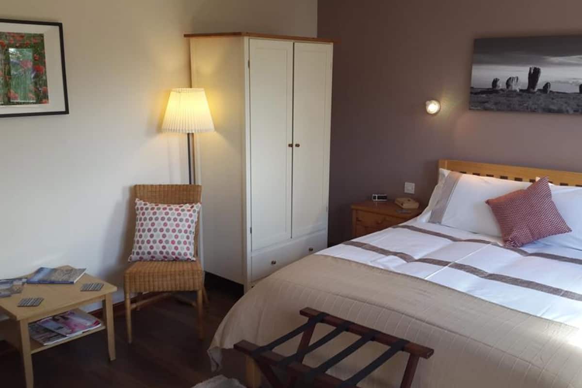 Habitación de hotel con cama, una silla, armario, mesita de noche y lámpara.