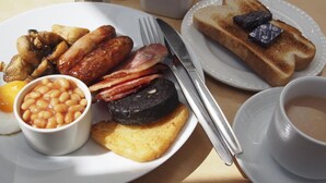 Een ontbijtbord met worstjes, spek, bonen, toast en een kop koffie.