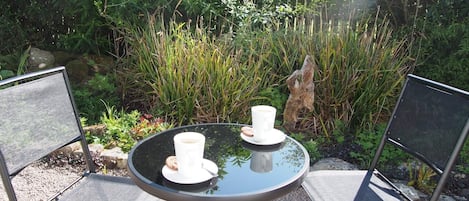 A round glass table with two chairs, a cup and saucer, and a cookie on the table.