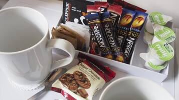 Uma bandeja com sachês de café, uma caneca, embalagem de biscoitos de chocolate belgas e um recipiente com leite.