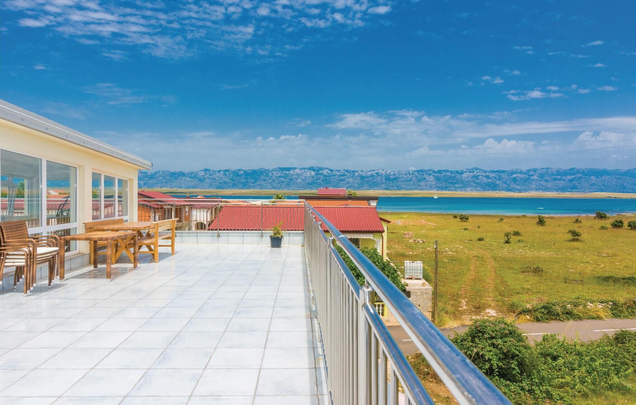 A balcony with a view of a lake and mountains, furnished with wicker chairs and a table.