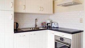Eine Küche mit weißen Schränken, einer schwarzen Arbeitsplatte, einer Edelstahl-Spüle, einer Kaffeemaschine, einem Toaster und einem Backofen.