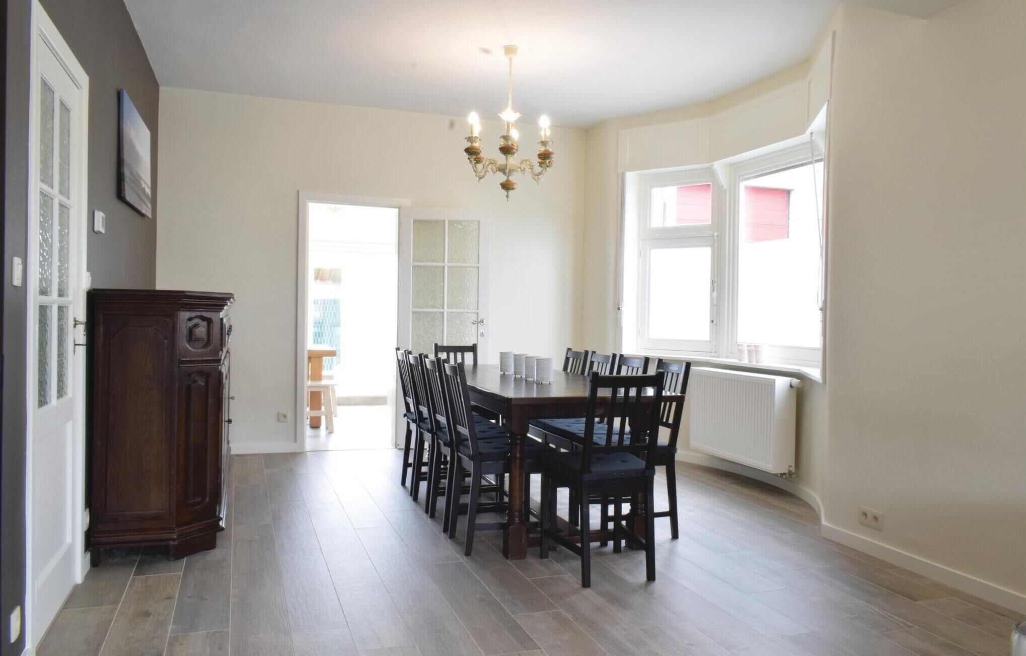 A dining area with a large table, multiple chairs, a chandelier, and a view of the outside.