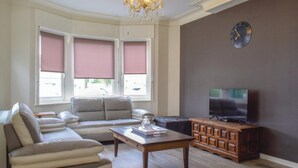 Ein Wohnzimmer mit einer Couch, einem Couchtisch, einem Fernseher und einem großen Fenster mit Jalousien.