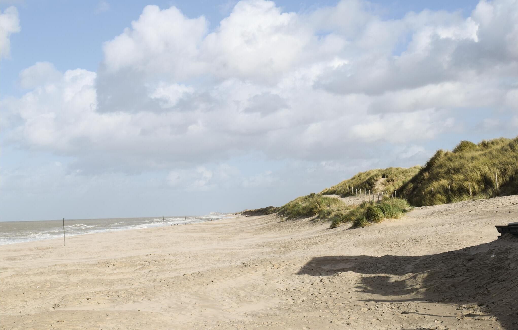Une plage de sable avec des dunes et un ciel dégagé.