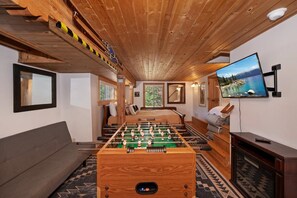 Una habitación con mesa de fútbol, sofá, televisor y chimenea.