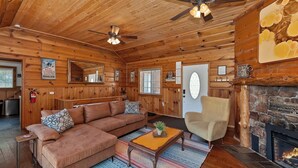 Ein gemütliches Blockhausschlafzimmer mit Holzbalkendecke, Kamin, einer Couch, einem Sessel und einem Couchtisch.