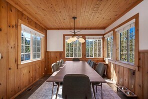 Una habitación con paneles de madera, una mesa grande y sillas, ventanas amplias y un ventilador de techo.