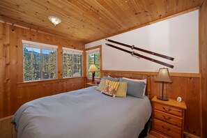 Un dormitorio con paneles de madera, una cama, mesitas de noche y una ventana con vistas a árboles.
