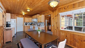 Innenansicht einer Holzhütte mit Küche, Essbereich und großen Fenstern.