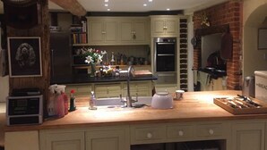 A kitchen with a wooden countertop, a sink, cabinets, a clock, and a brick wall. - Waldegrave farm (Bury St Edmunds)