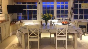 A dining area with a table set for four, surrounded by white chairs. There is a vase with flowers on the table, and a bowl of oranges on the right side. - Waldegrave farm (Bury St Edmunds)
