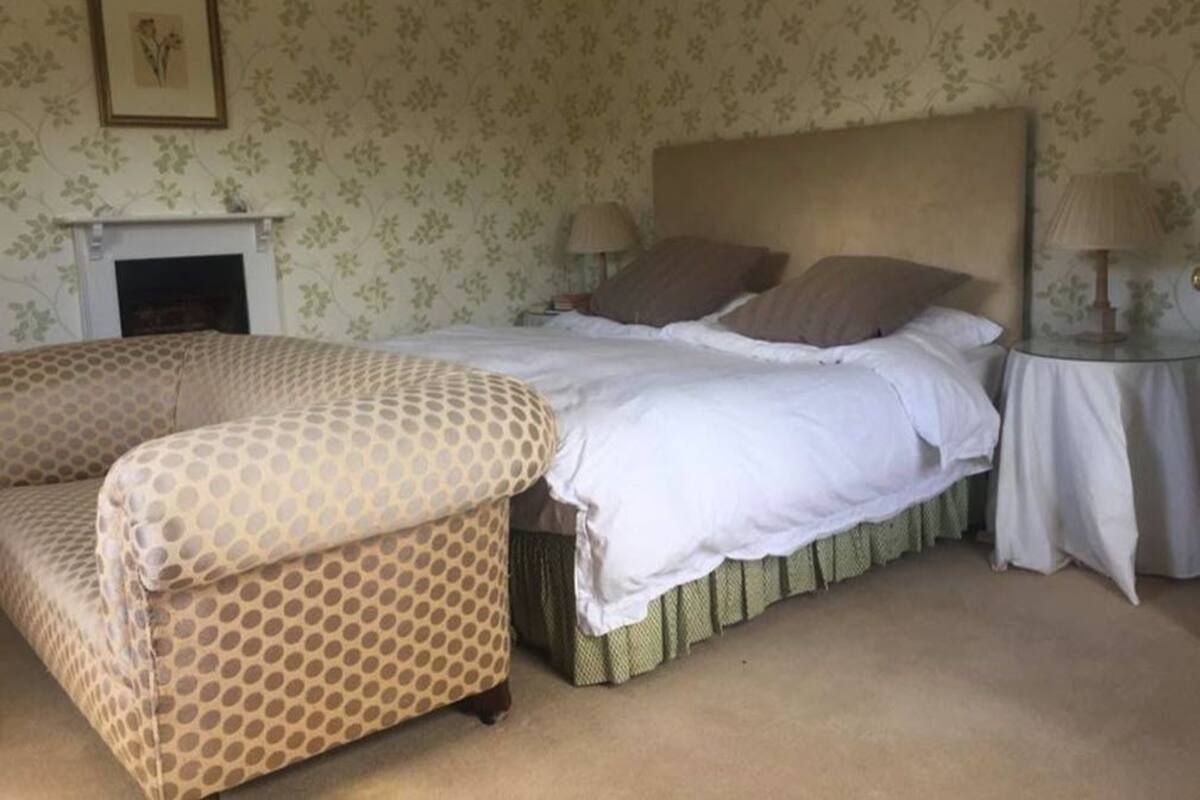 Ein Schlafzimmer mit einem Bett, einem Sessel, einem Nachttisch und einem Kamin.