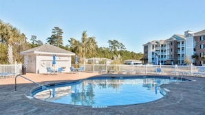 A swimming pool with lounge chairs and a small building, surrounded by a fence and trees. -  Beautiful, Clean condo, new furniture beds carpet TVs. Lake view, private Wifi  (Myrtle Beach)