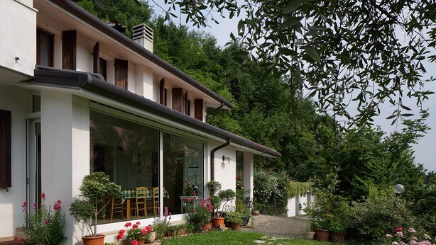 A house with a covered patio, potted plants, and a garden path. - B&B La Casa in Collina (Sarmede)