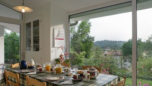 A dining area with a table set for breakfast, a view of greenery and houses outside, and a calendar on the wall. - B&B La Casa in Collina (Sarmede)