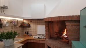 A kitchen with a brick fireplace, a gas stove, and a hanging pot rack. - B&B La Casa in Collina (Sarmede)
