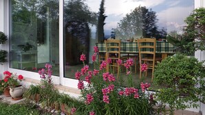 A conservatory with a glass wall, a wooden table with chairs, and various potted plants and flowers. - B&B La Casa in Collina (Sarmede)