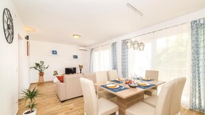 A modern living room with a dining area, wooden flooring, and large windows with patterned curtains. - Gorgeous home in Kastel Novi with WiFi (Kastel Novi)