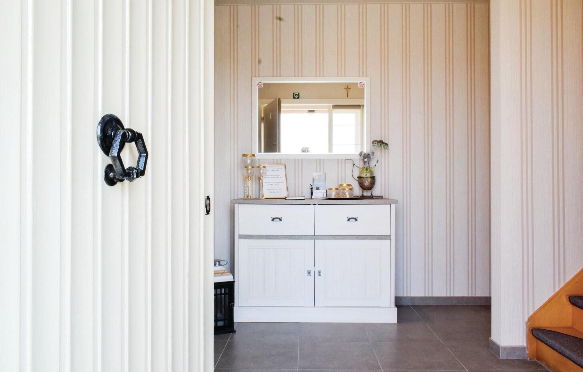 A hallway with a white door, a white cabinet with drawers, and a mirror above it.