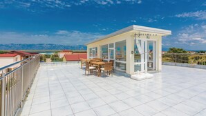 A rooftop terrace with a dining area, a small service booth, and a view of mountains and a body of water. - 1 bedroom cozy apartment in Vir (Vir)