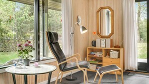 A modern room with a large window, a black leather chair, a small wooden table, a bookshelf, and a mirror on the wall. - 3 bedroom awesome home in Vejers Strand (Vejers Strand)