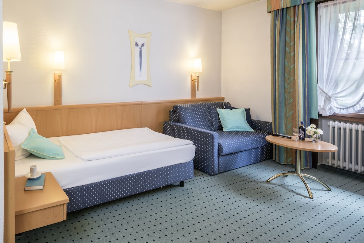 Quarto de hotel com duas camas, um sofá, uma mesinha e uma janela com cortinas.