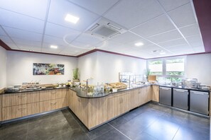 A modern kitchen with a curved counter, stainless steel appliances, and a large window providing natural light. - Hotel Monika (Buettelborn)