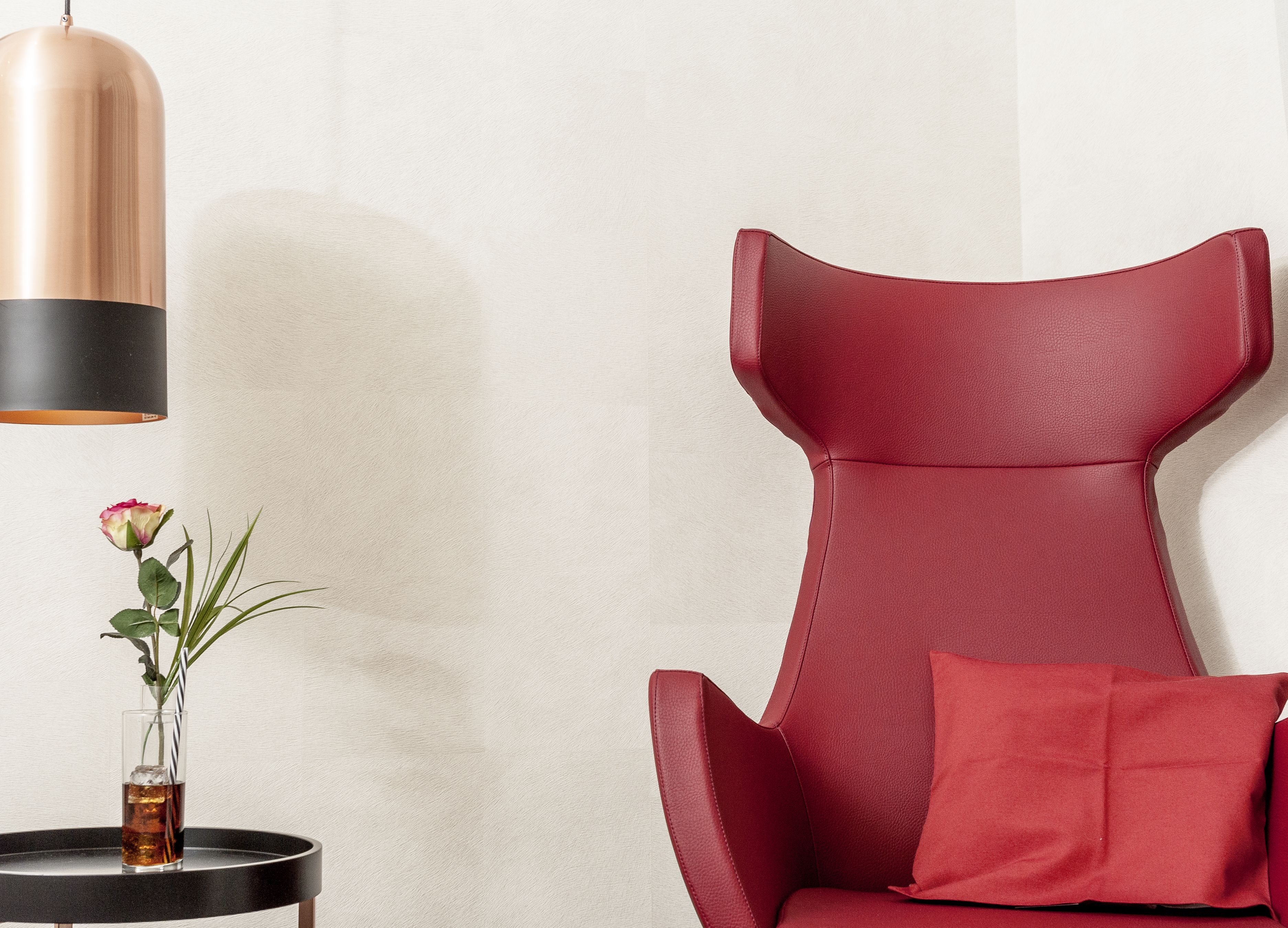 A red leather chair with a cushion, a small table with a vase of flowers, and a pendant light.