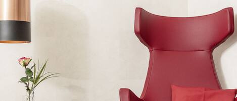 A red leather chair with a cushion, a small table with a vase of flowers, and a pendant light.