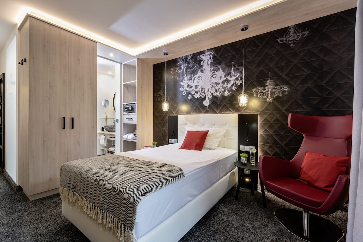 Quarto moderno com uma cama grande, uma poltrona vermelha, um guarda-roupa e um candelabro fixado na parede.