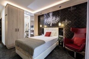 A modern bedroom with a large bed, a red armchair, a wardrobe, and a wall-mounted chandelier. - Hotel Monika (Buettelborn)