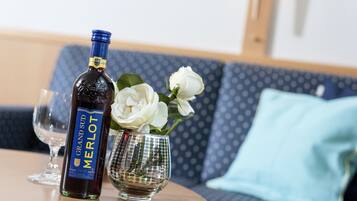 A bottle of Grand Sufi Merlot wine, a glass, and a vase with white flowers on a round table.