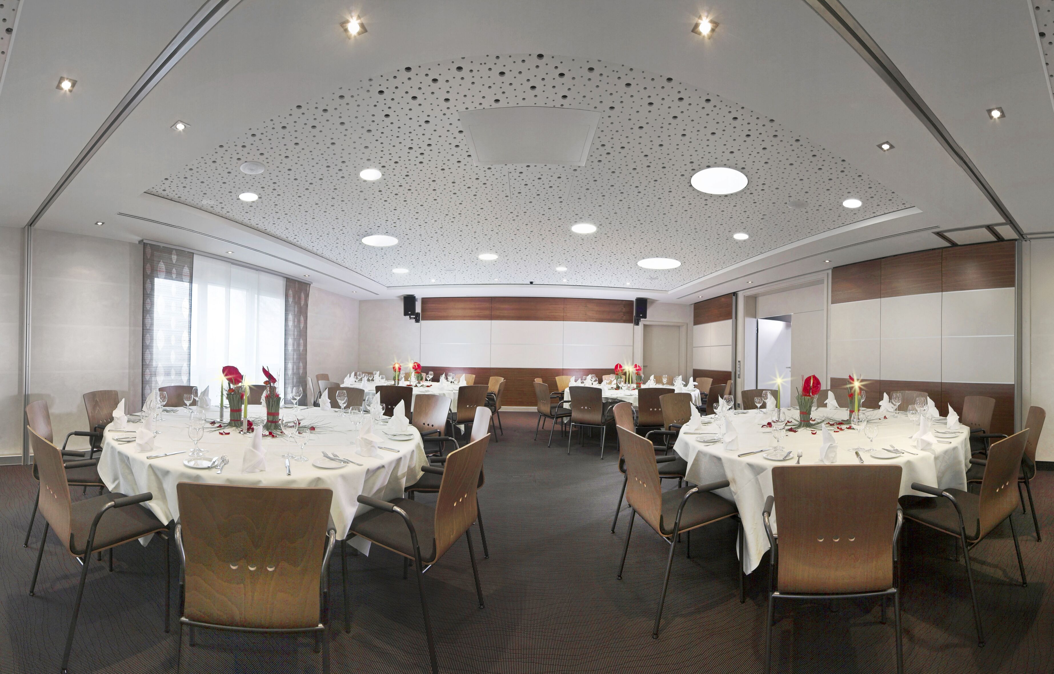 A conference room with multiple round tables, each set with white tablecloths, chairs, and dining essentials.