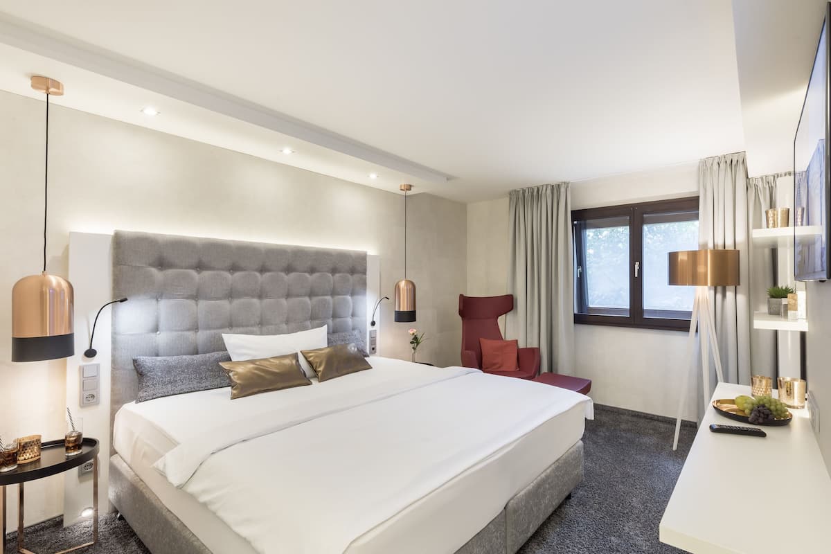 Quarto de hotel moderno com uma cama grande, uma escrivaninha com computador e uma janela com cortinas.